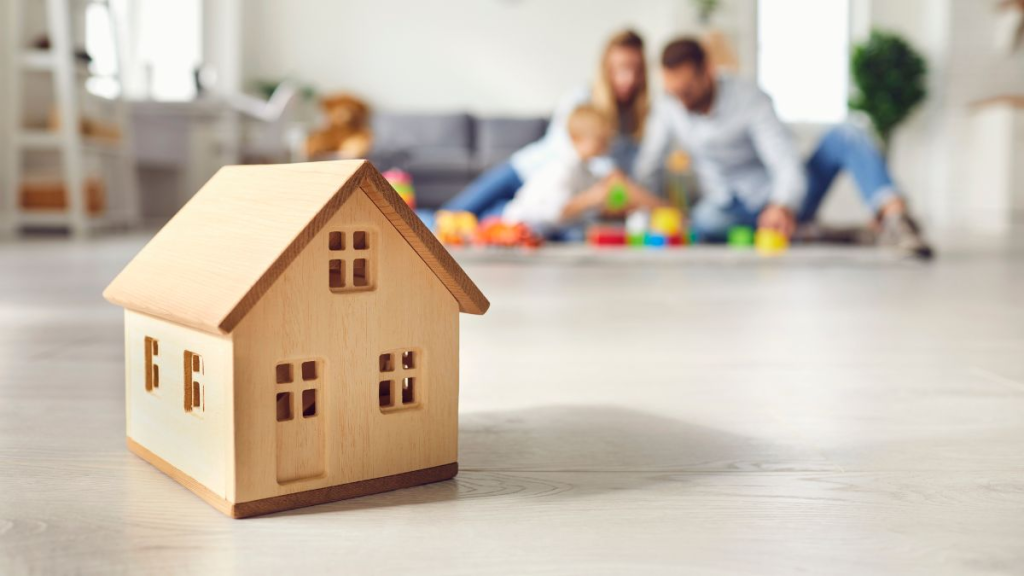 Casa de madera de juguete con una familia en su nueva vivienda al fondo
