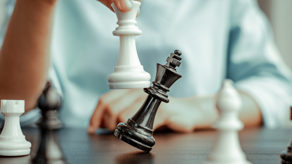 Mano derribando rey negro con pieza blanca de ajedrez sobre tablero, simbolizando estrategia
