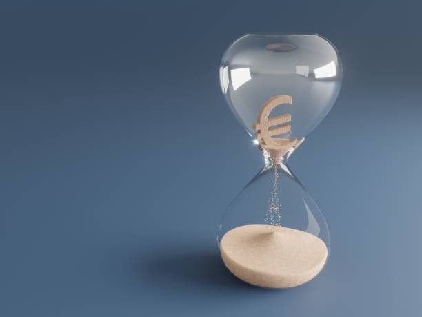 Reloj de arena de cristal sobre un fondo azul con un símbolo del euro tridimensional en la parte superior deshaciéndose en forma de arena hacia la base, representando el coste del paso del tiempo.