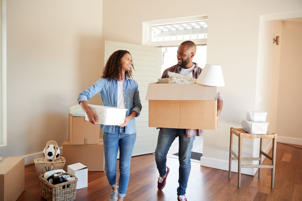 Pareja joven sonriente cargando cajas durante la mudanza a su nueva vivienda