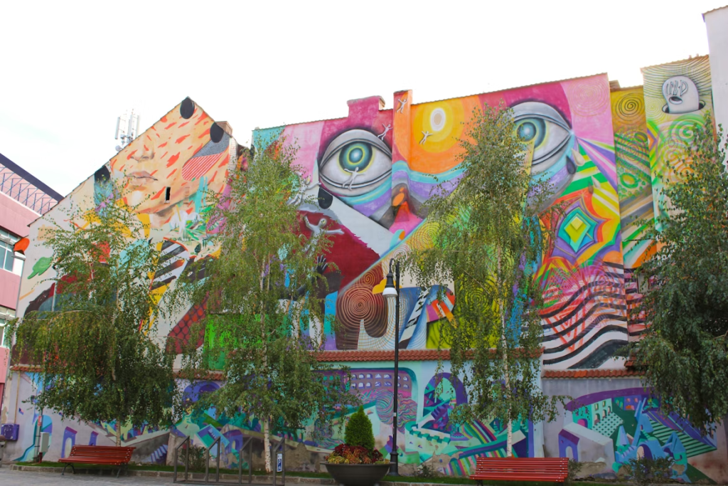 Gran mural de arte urbano con figuras y colores vivos en la fachada de un edificio de barrio