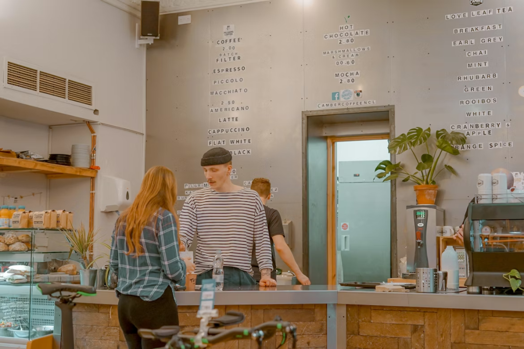 Interior de cafetería de barrio con barra de madera, carta en pared y clienta siendo atendida