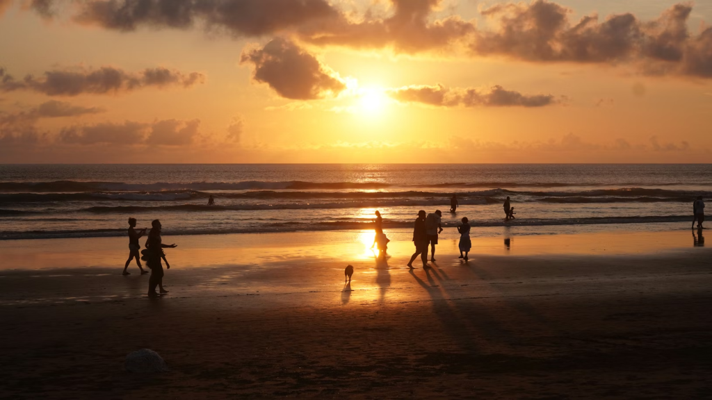 Siluetas de personas paseando por la orilla de la playa durante un atardecer dorado