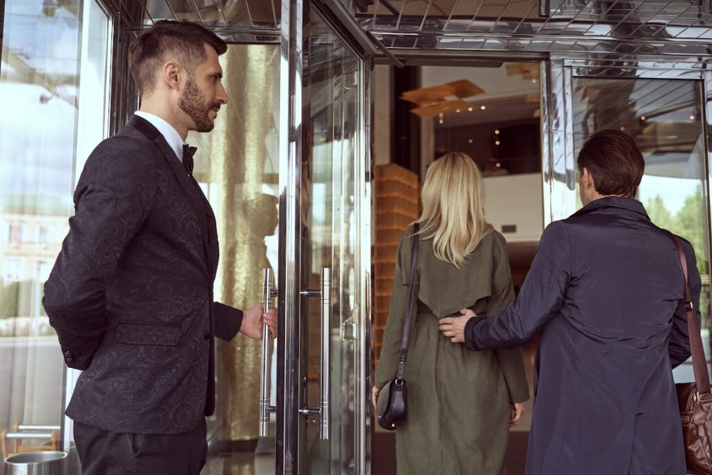 Pareja entrando a edificio de lujo con portero abriendo la puerta en zona residencial de alto standing