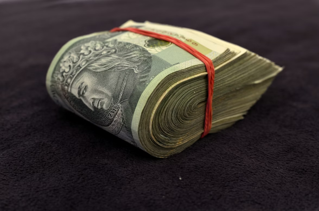 Fajo grueso de billetes enrollados y sujetos con goma elástica sobre superficie oscura