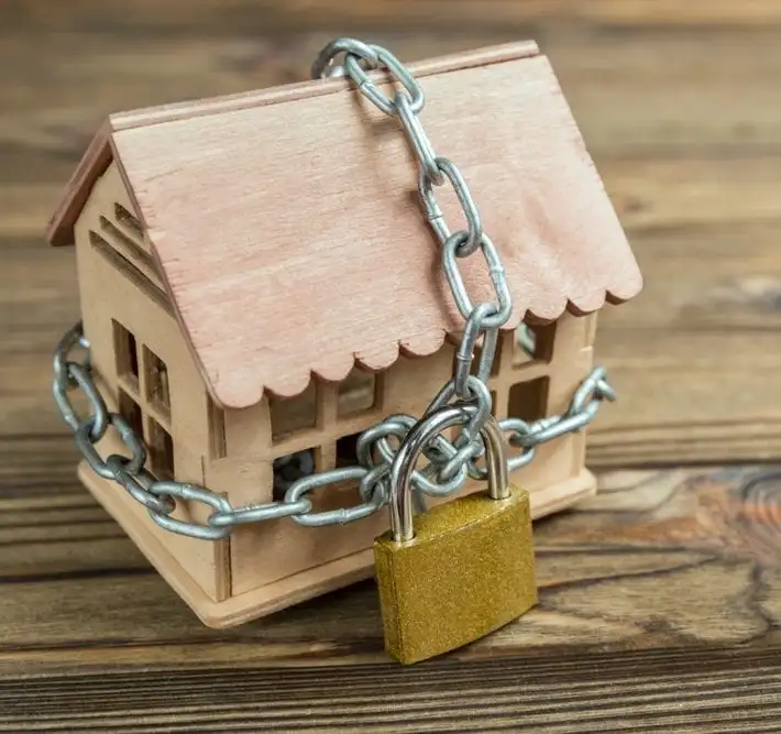 Maqueta de casa de madera encadenada con candado sobre superficie de madera