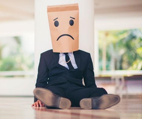 Hombre de traje en el suelo con una bolsa triste en la cabeza por problemas hipotecarios