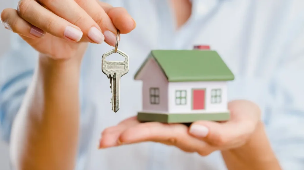 Manos de mujer sosteniendo llave y maqueta de casa simbolizando entrega de vivienda en compraventa.