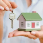Manos de mujer sosteniendo llave y maqueta de casa simbolizando entrega de vivienda en compraventa.