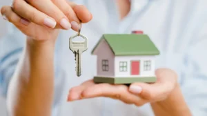 Manos de mujer sosteniendo llave y maqueta de casa simbolizando entrega de vivienda en compraventa.