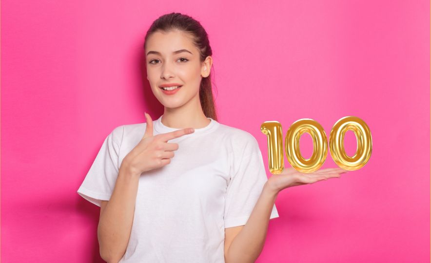 Mujer joven sonriendo y señalando el número 100 dorado en referencia a hipotecas al 100% de financiación
